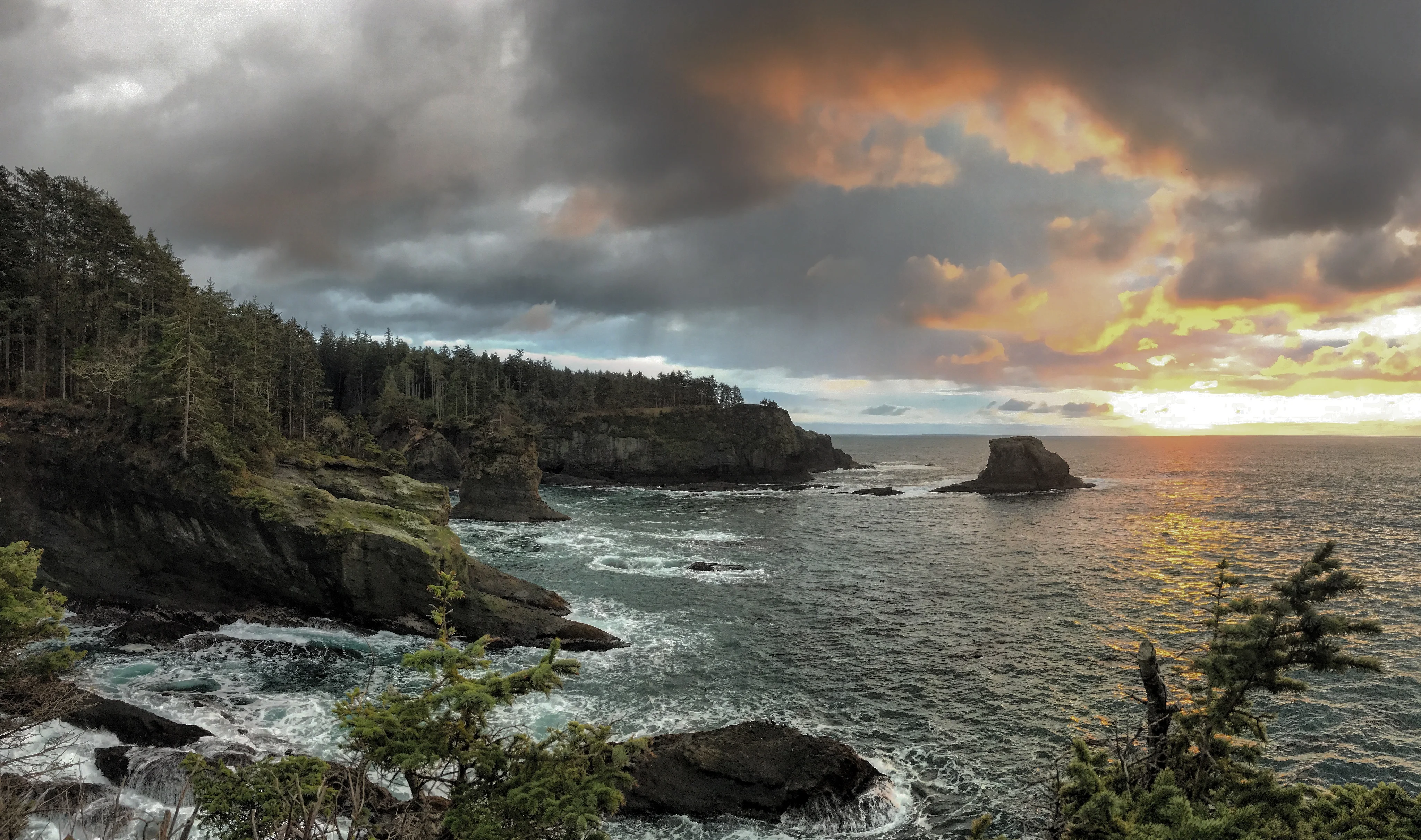Sunset light breaks through clouds above the rugged coastline and sea stacks at Cape Flattery.